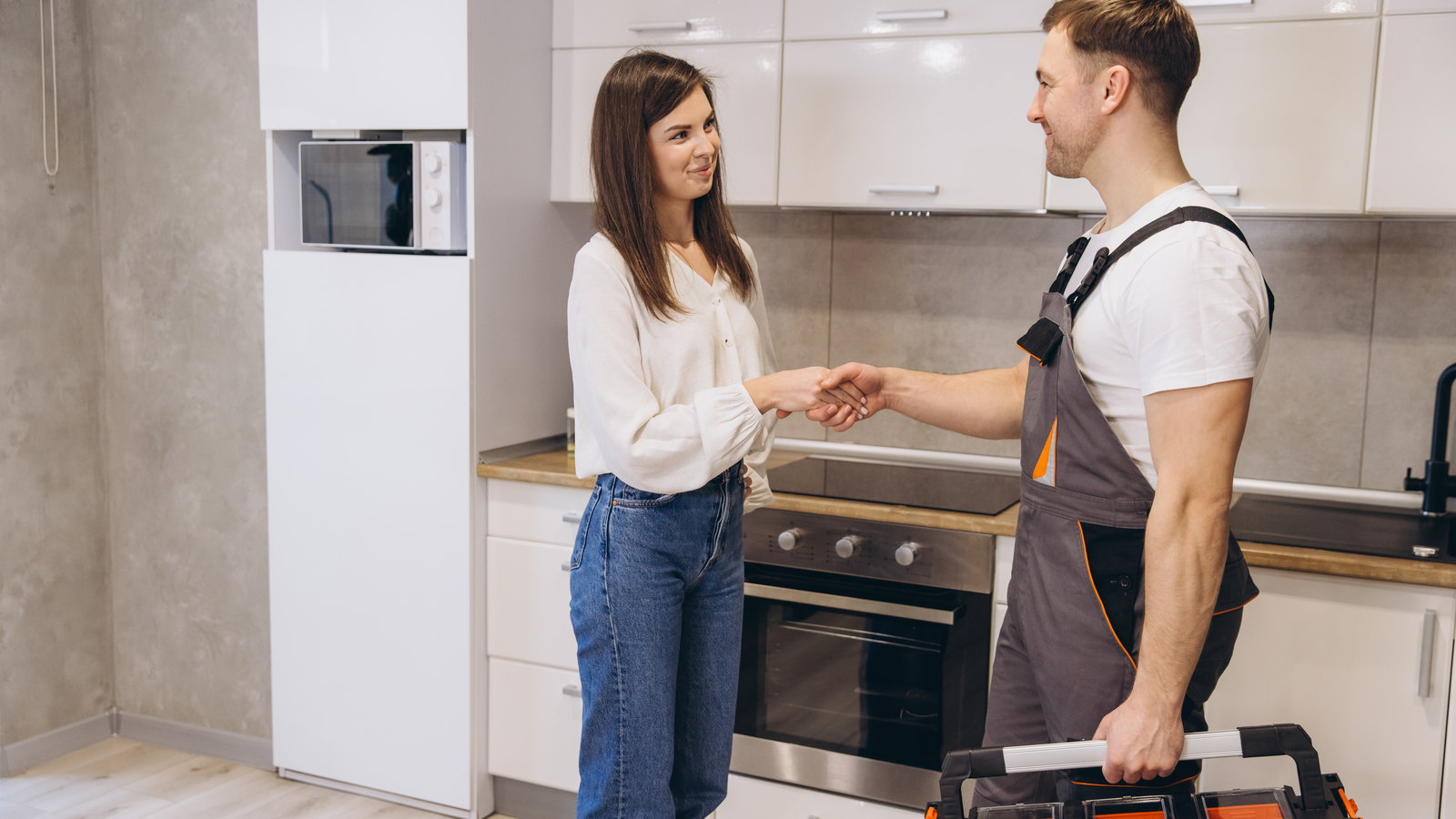 Plumber shaking hands with a homeowner in her kitchen after finishing a job